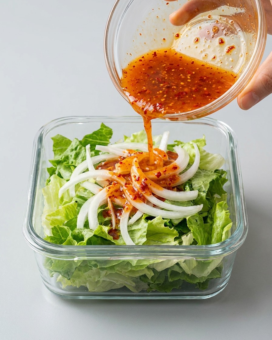 Rote Kimchi-Brühe wird über den geschichteten Salat und die Zwiebeln gegossen.