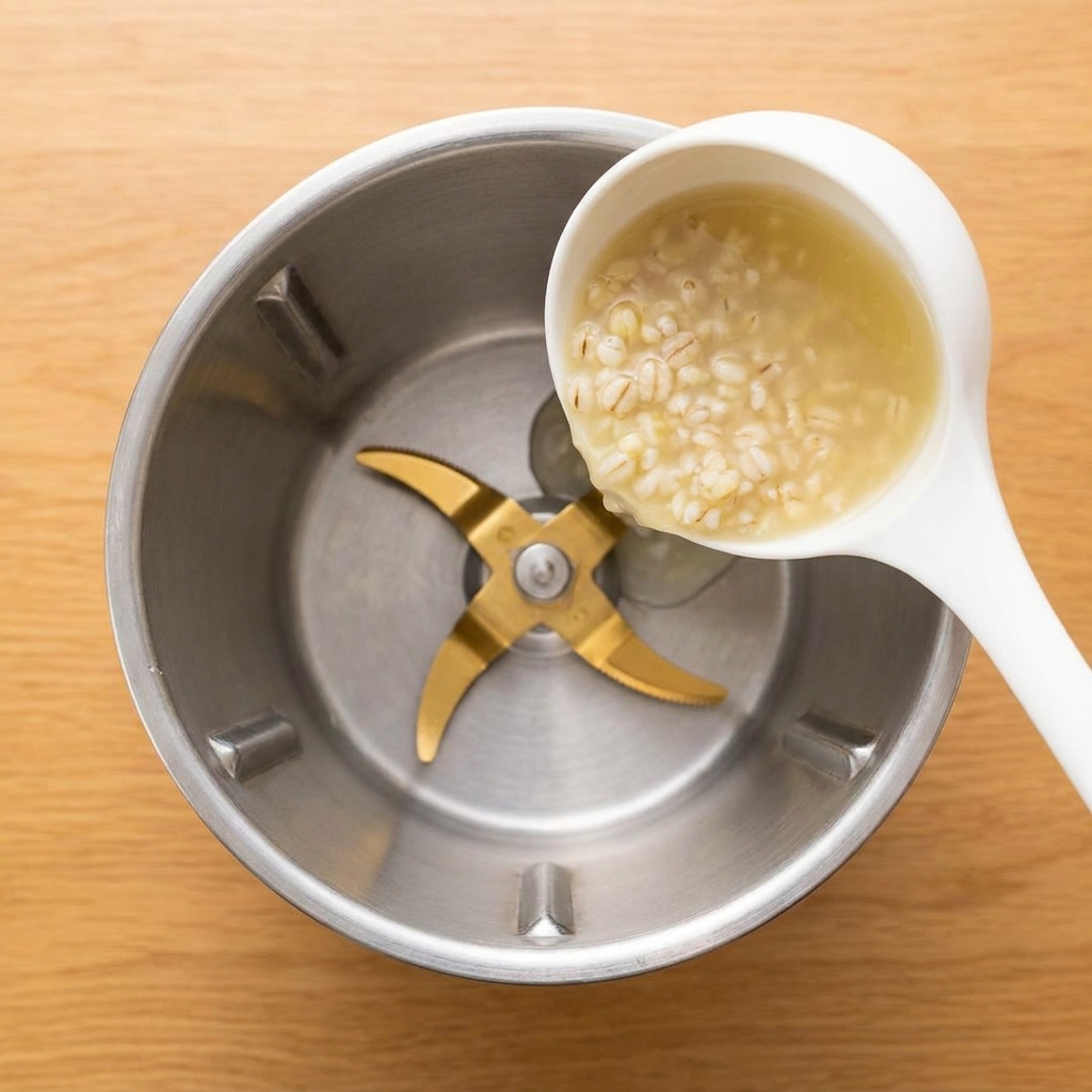 Heller Gerstenbrei wird mit einer Kelle in einen Standmixer gefüllt.