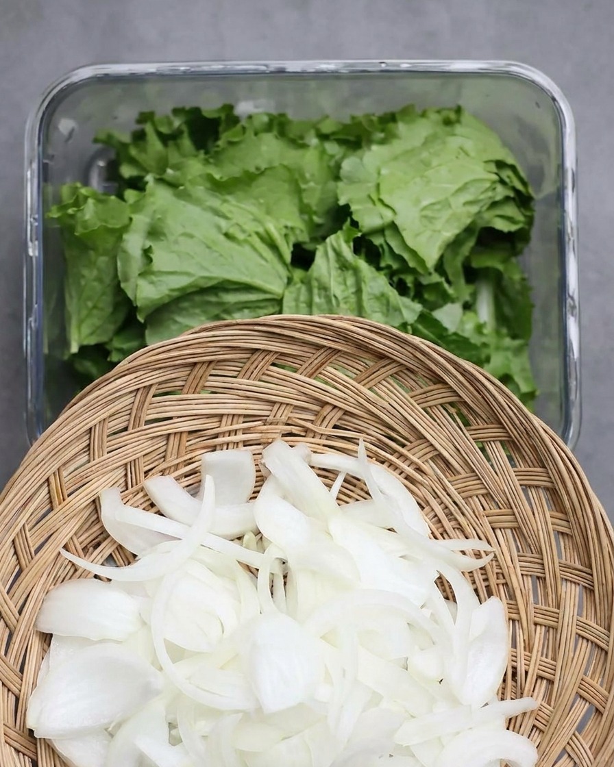 Dünne Zwiebelscheiben werden über frische Salatblätter im Behälter verteilt.