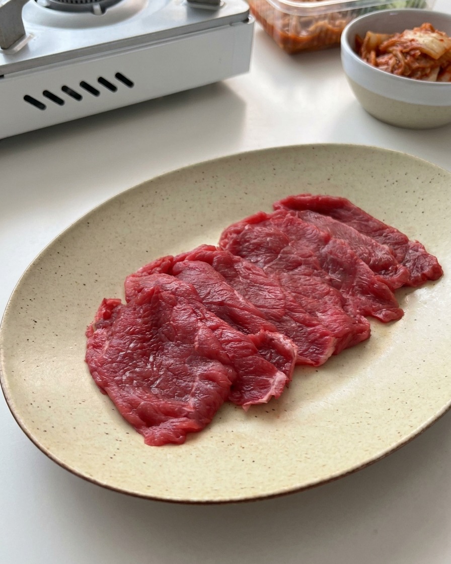 Hauchdünn geschnittenes rohes Rindfleisch gleichmäßig auf einem hellen Keramikteller angerichtet.