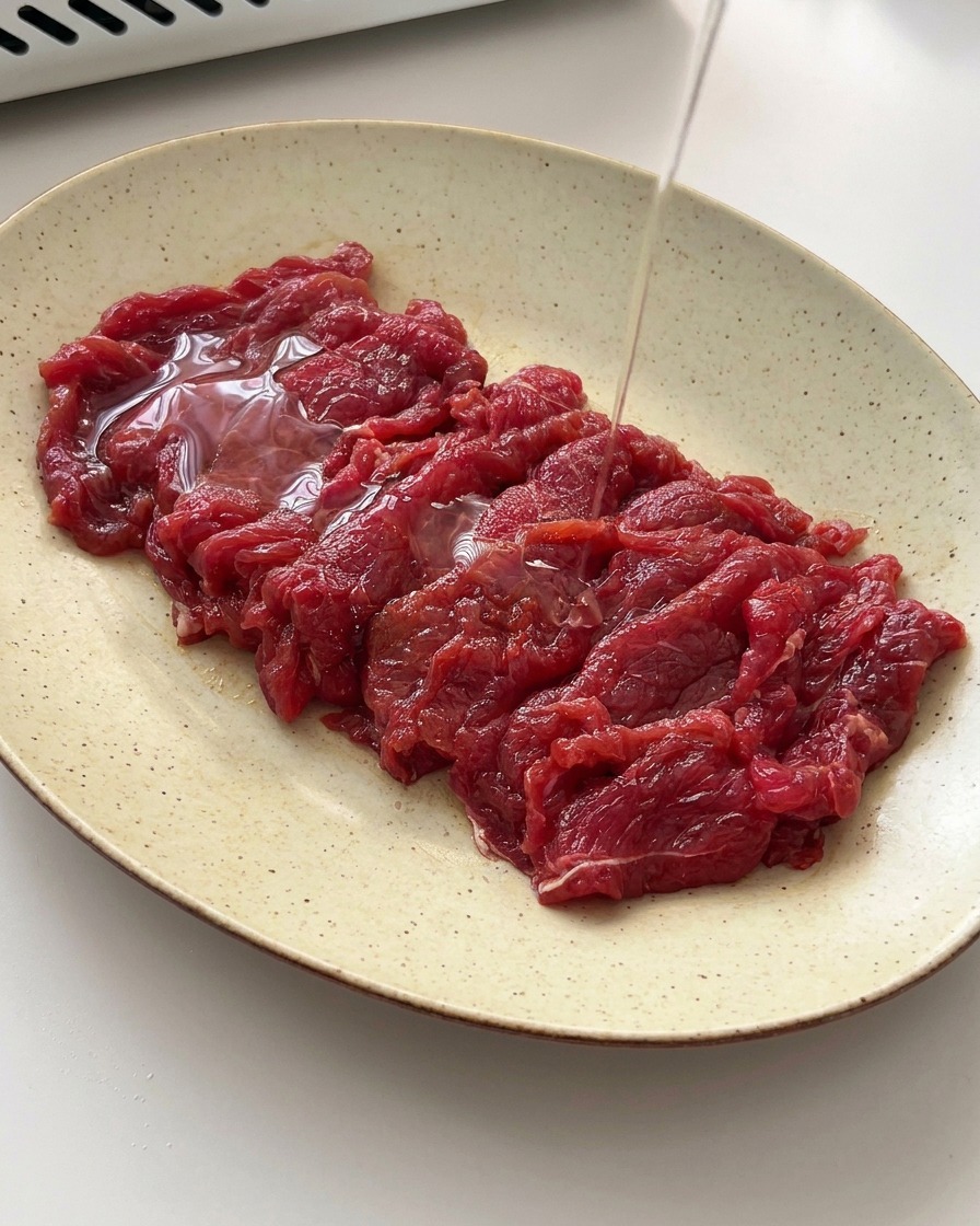 Ein feiner Strahl Speiseöl wird über das marinierte Rindfleisch gegossen.