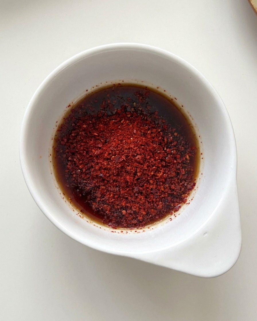 Eine kleine weiße Schüssel mit einer Mischung aus Sojasauce und leuchtend rotem Chilipulver.