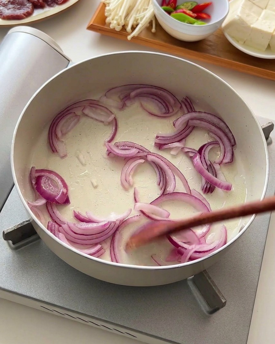 Rote Zwiebelringe werden mit einem Holzlöffel in einer flachen weißen Pfanne angebraten.
