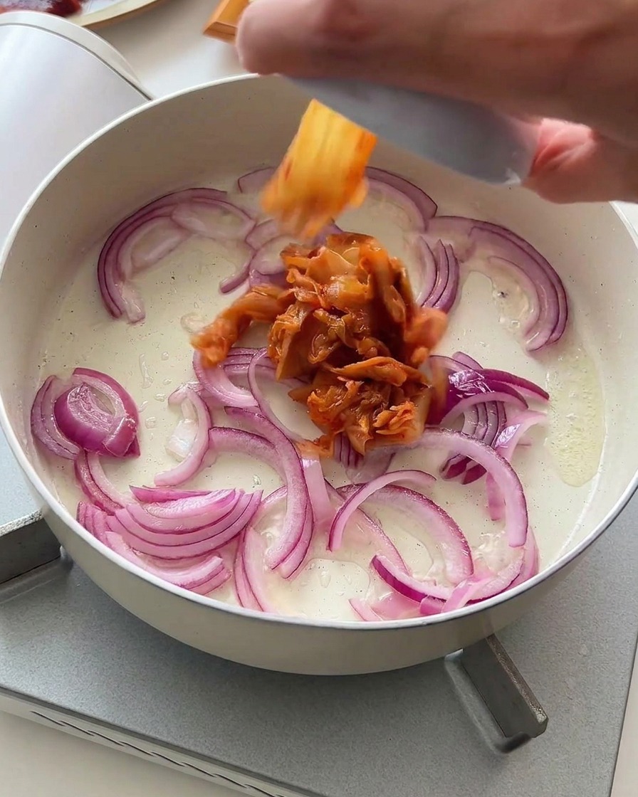 Gehacktes Kimchi wird zu den bratenden Zwiebeln in die Pfanne gegeben.