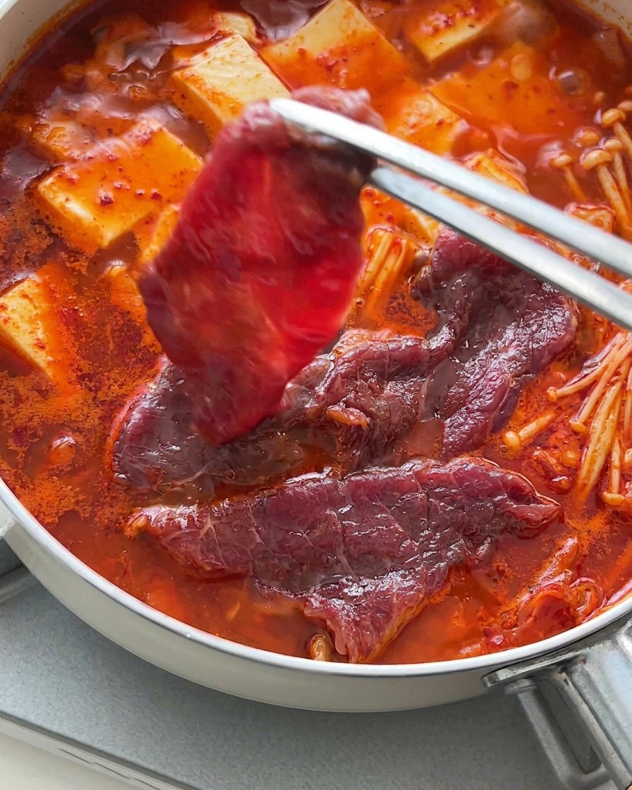 Eine Zange legt dünne Scheiben rohes Rindfleisch über den kochenden Eintopf mit Tofu.