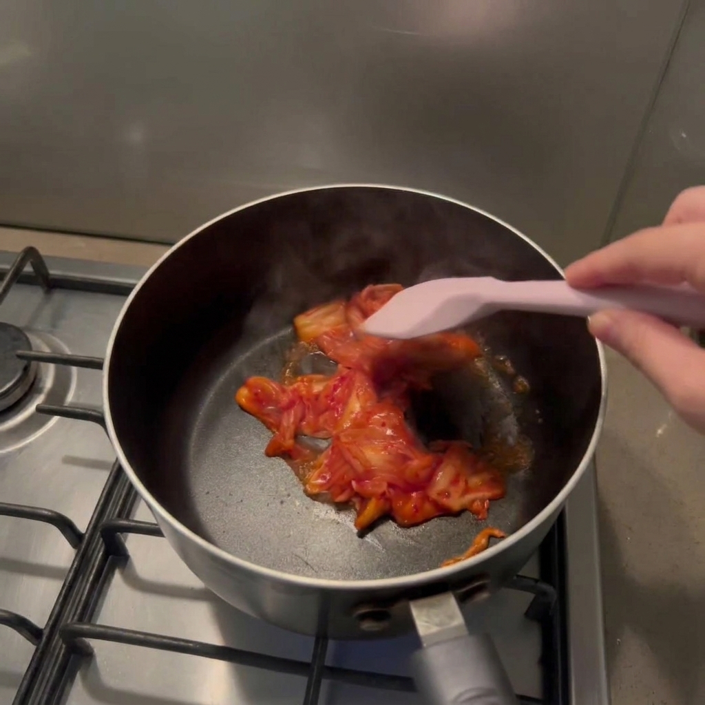 Ein Pfannenwender rührt kleingeschnittenes rotes Kimchi in einem schwarzen Topf um.