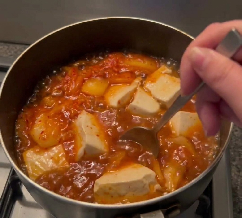 Sojasauce wird in die kochende Kimchi-Suppe mit Tofu gegeben.