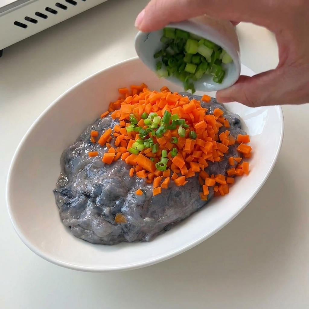 Fein gewürfelte orangefarbene Karotten werden in eine weiße Schüssel mit grauer, roher Garnelenpaste gegeben.