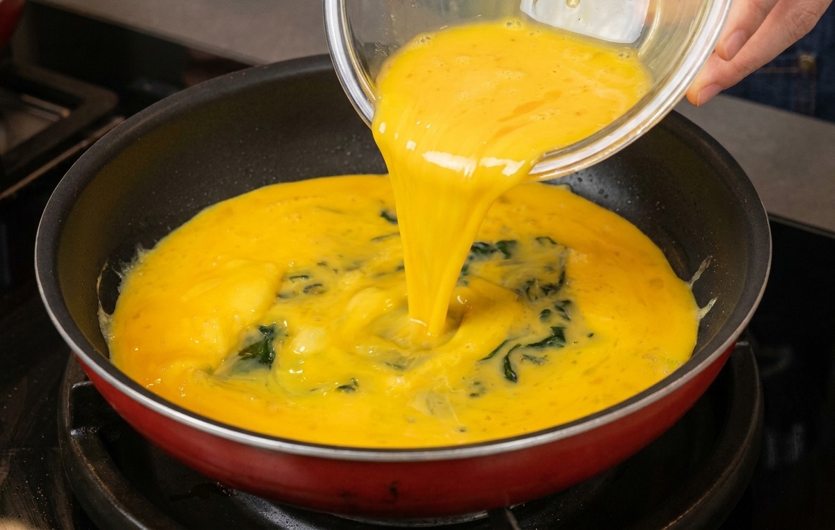 Die gelbe, verquirlte Eimischung wird aus einer Glasschüssel in eine saubere Bratpfanne gegossen.