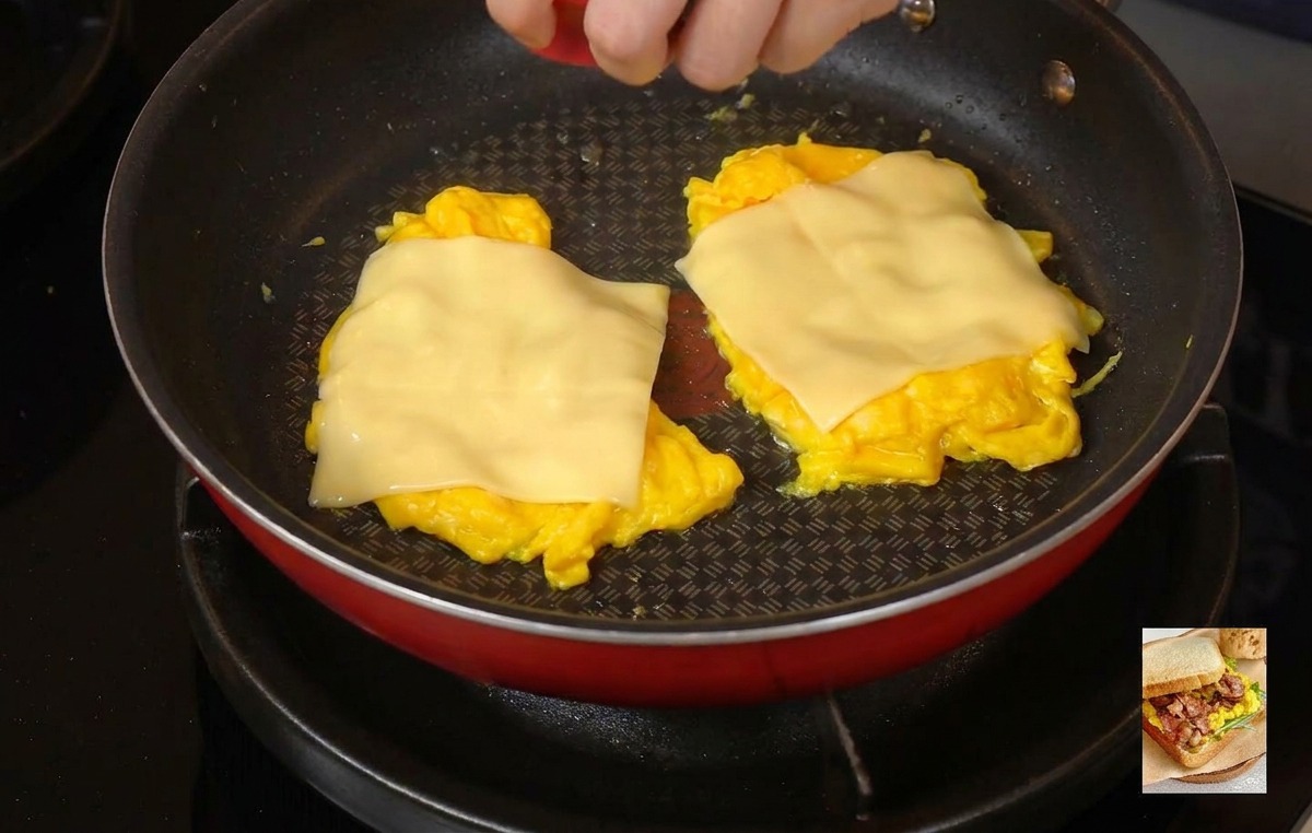 Eine Person setzt einen hellroten Deckel auf eine Pfanne, um Dampf einzuschließen und den Käse auf dem Rührei zu schmelzen.