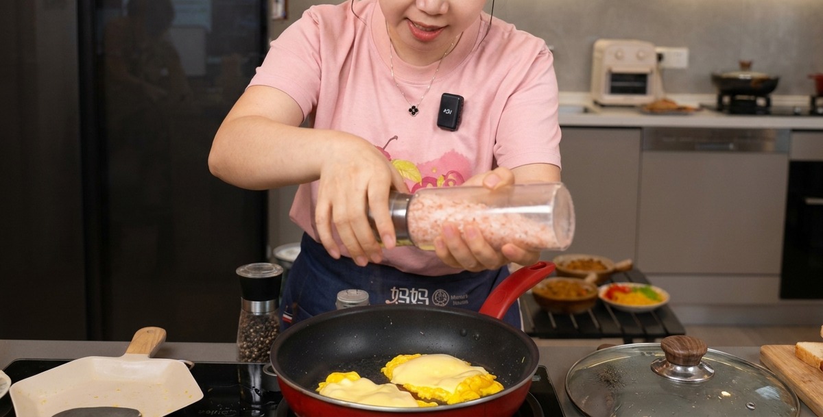 Eine Person mahlt Meersalz und schwarzen Pfeffer aus einer transparenten Mühle auf fluffiges Rührei mit geschmolzenem Käse.