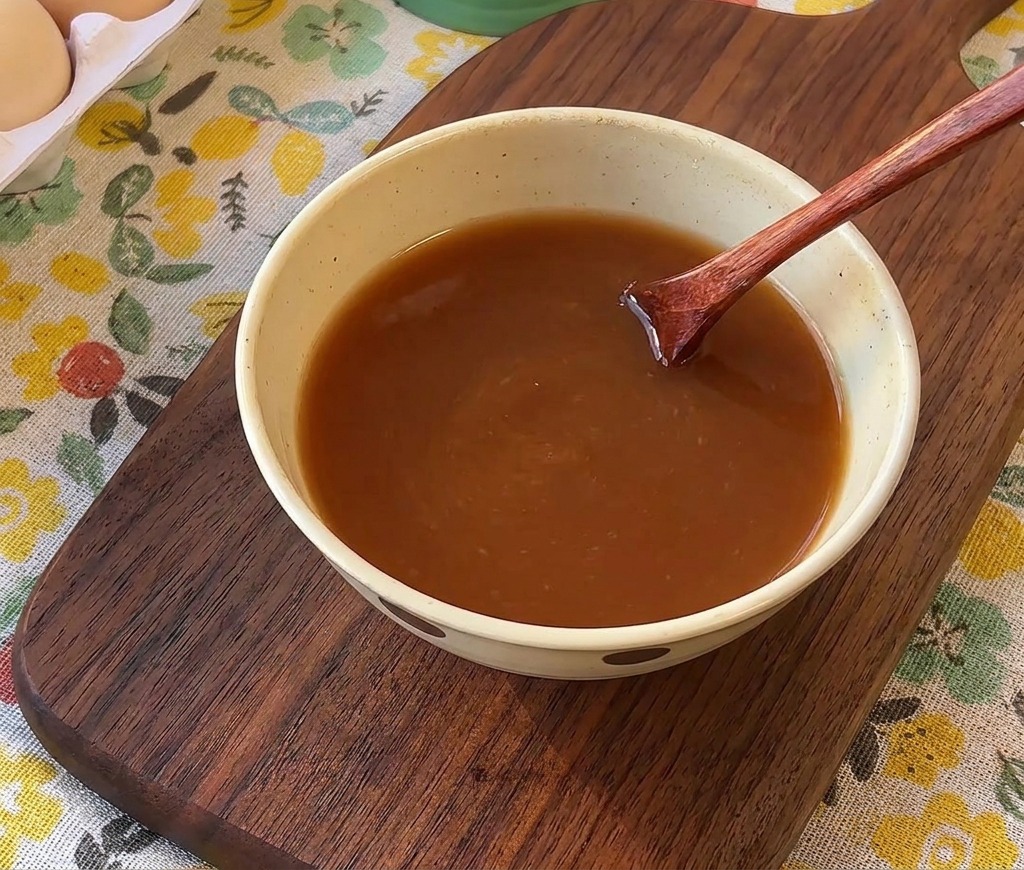 Ein Holzlöffel rührt eine braune Saucenmischung in einer kleinen Keramikschüssel um.