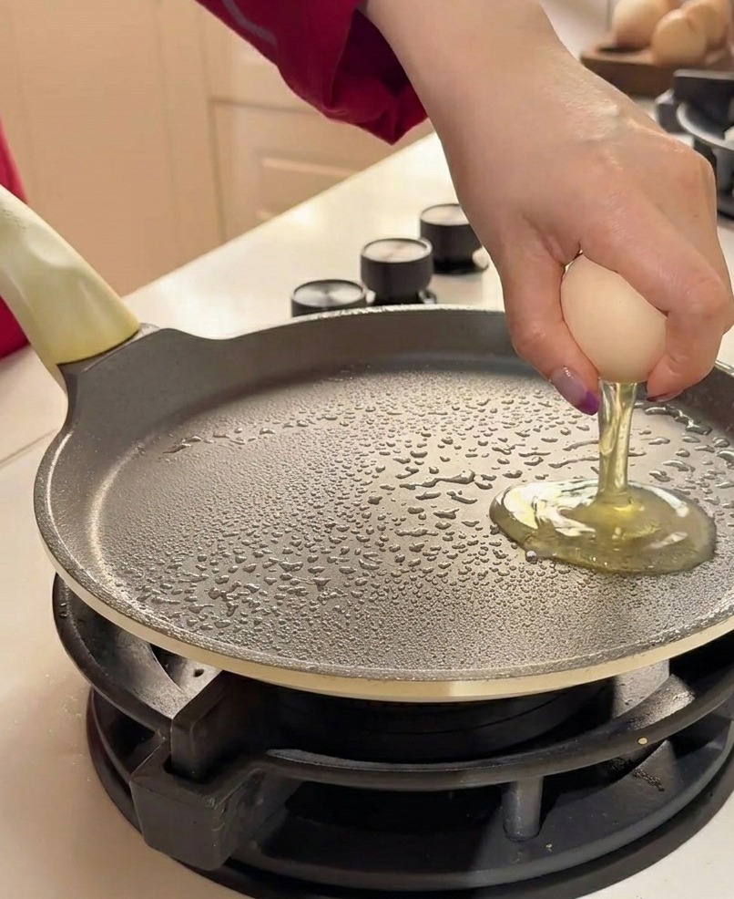 Zwei rohe Eier werden per Hand in eine leicht gefettete, flache Bratpfanne geschlagen.