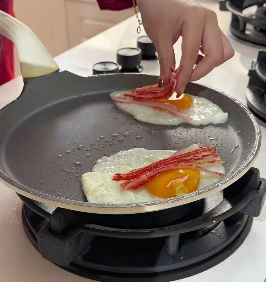 Eine Hand platziert feine Streifen von zerkleinertem Surimi auf die garenden Eier in der Pfanne.