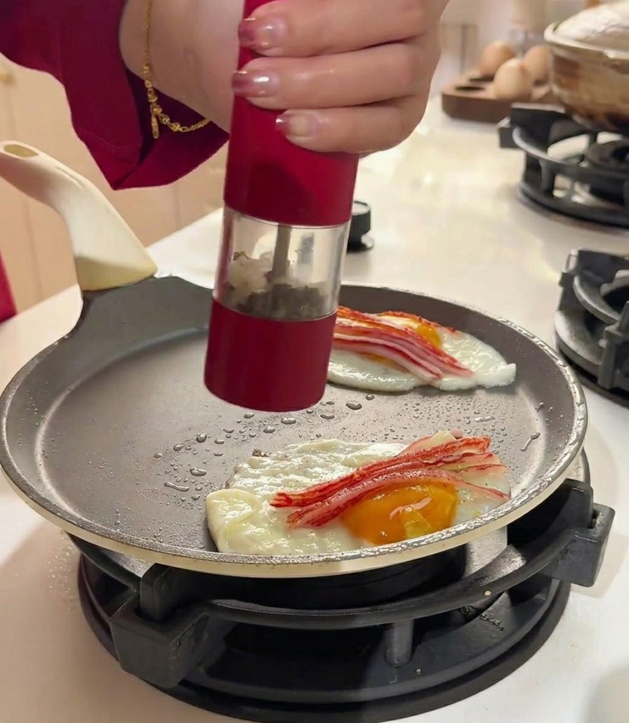 Eine Pfeffermühle würzt die Eier und das Surimi in einer flachen Bratpfanne.