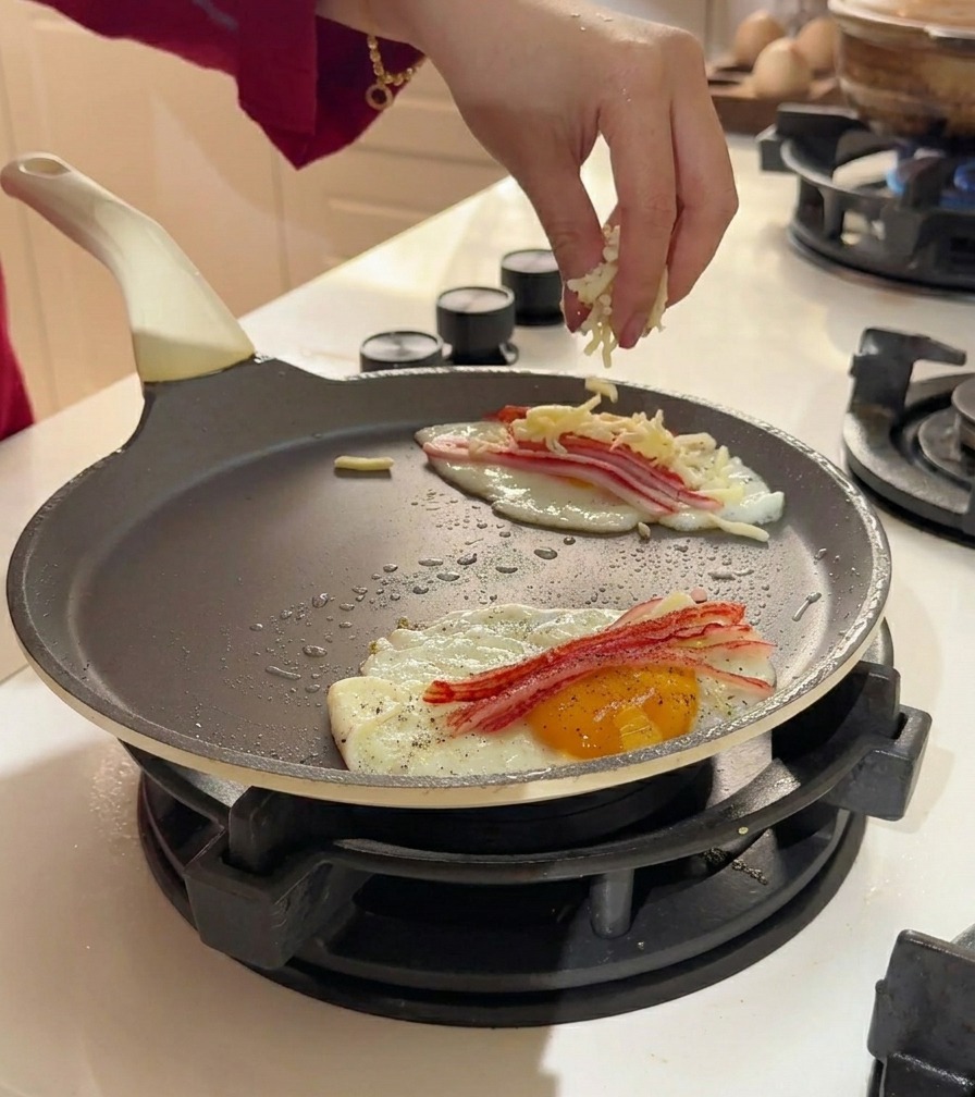 Geriebener Käse wird großzügig über die Eier und das Surimi in der Pfanne gestreut.