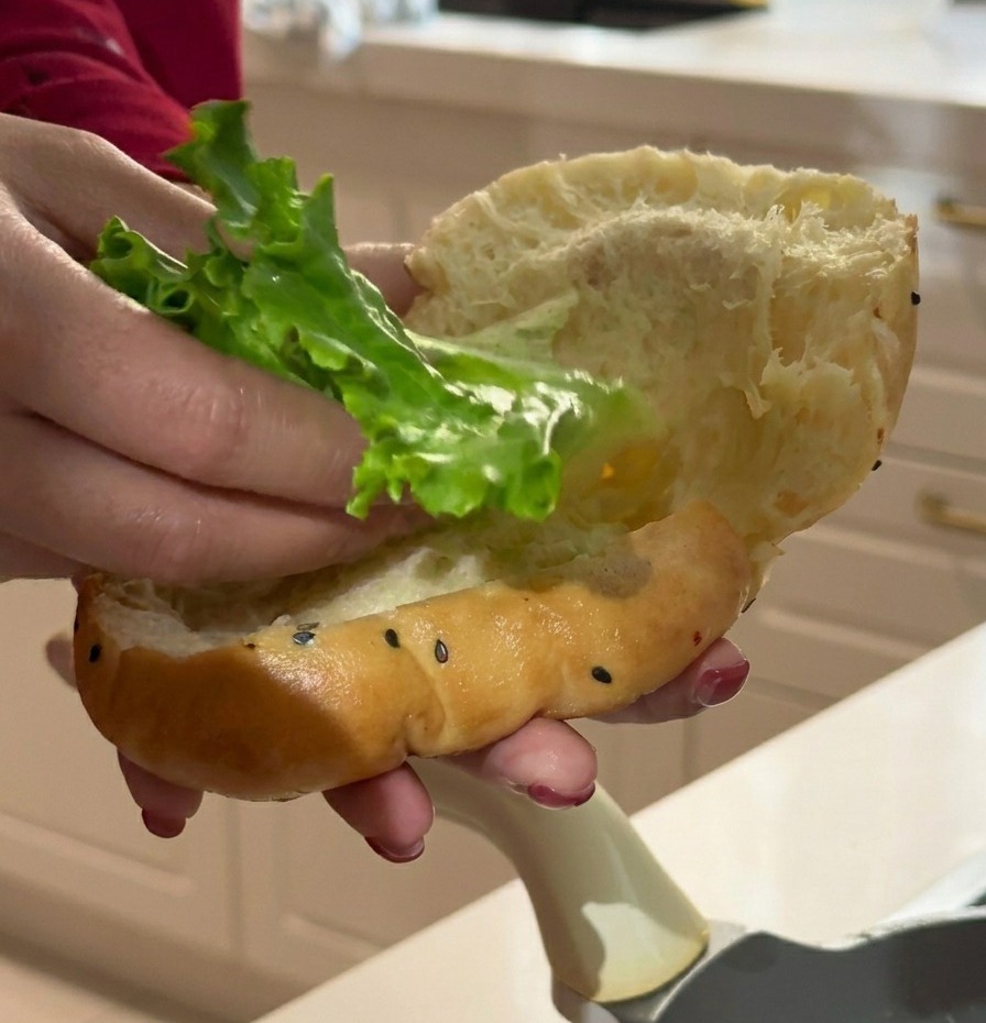 Ein Blatt krauser grüner Salat wird in das weich aufgeschnittene Brötchen gesteckt.