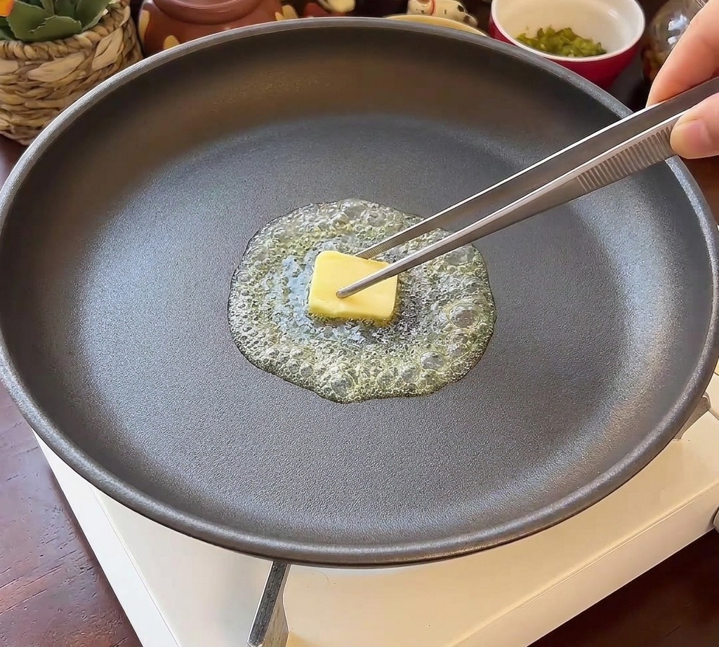 Zwei Burgerbrötchen-Hälften liegen mit der Schnittseite nach unten in einer Pfanne mit glänzender Butter.