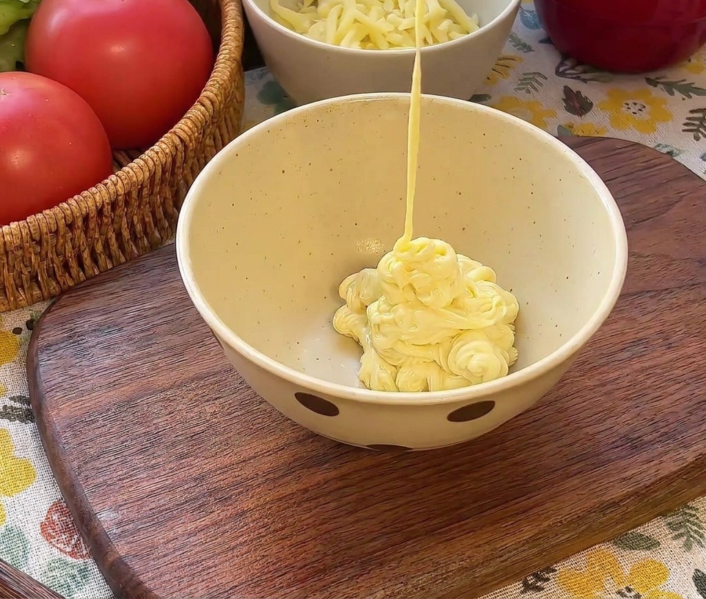 Cremige Mayonnaise wird in eine Schüssel über roten Ketchup und grüne, gehackte Gurken gegossen.