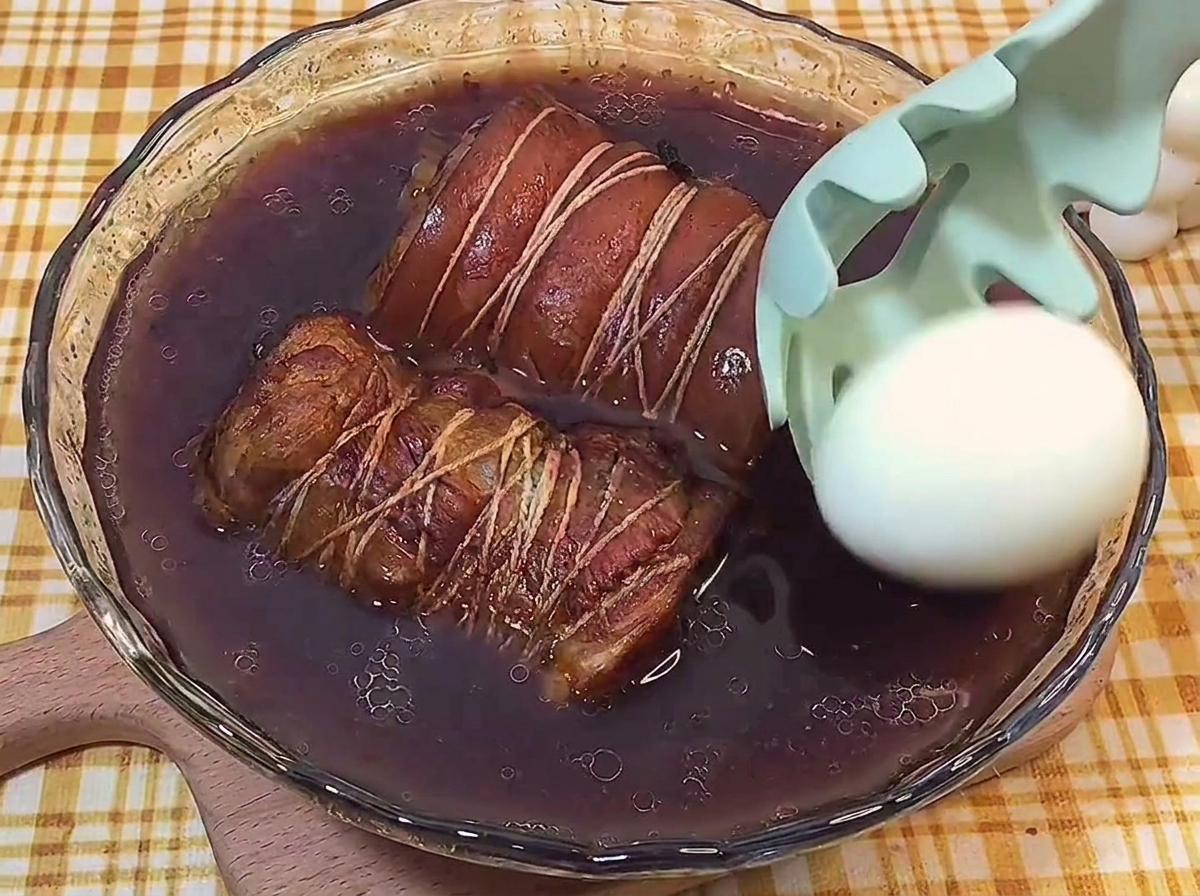 Ein geschältes, hartgekochtes Ei wird mit einem Schaumlöffel in den dunklen Sud zum Fleisch gelegt.