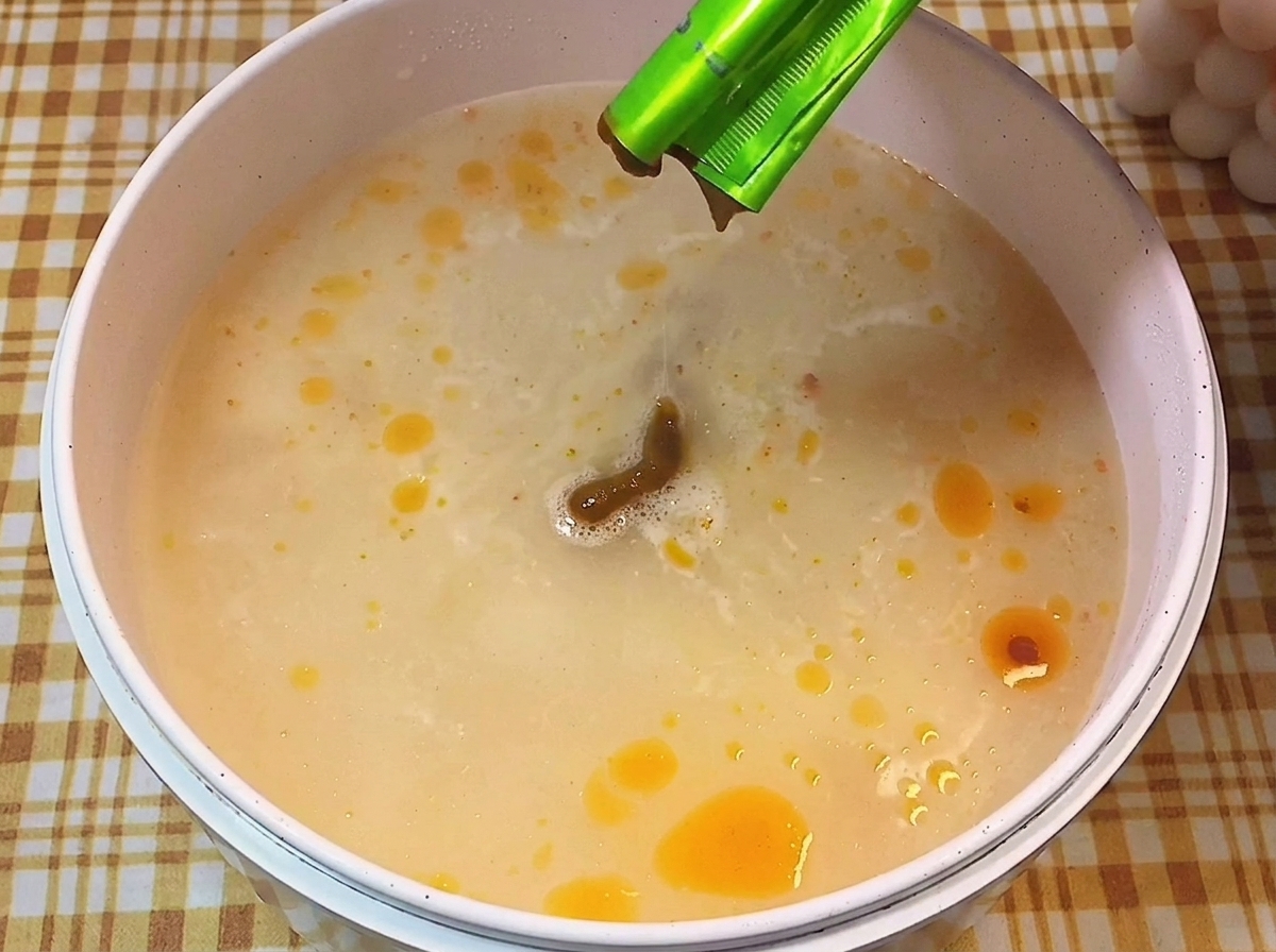 Braune Würzpaste wird in einen Topf mit siedender, milchiger Brühe gegeben.