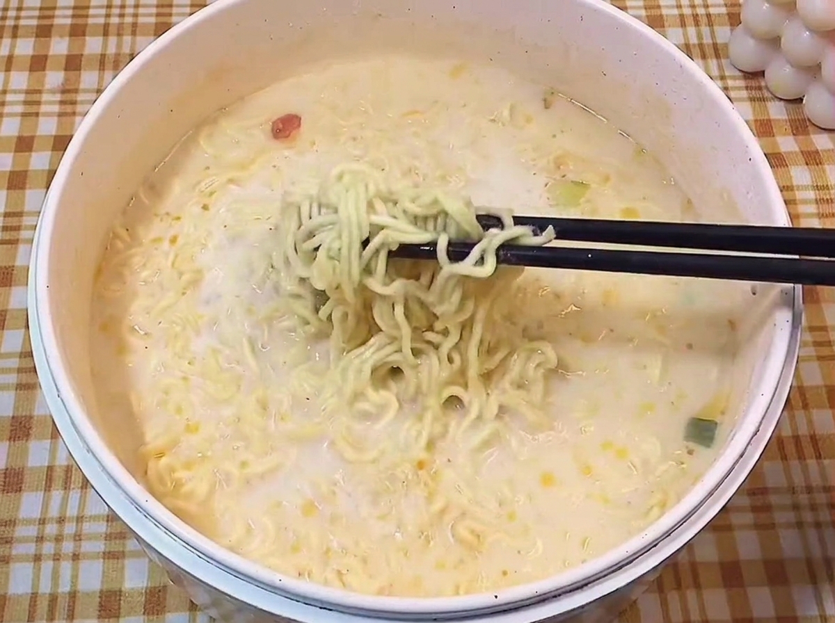 Schwarze Essstäbchen heben eine Portion gewellte Ramen-Nudeln aus der cremigen Brühe.