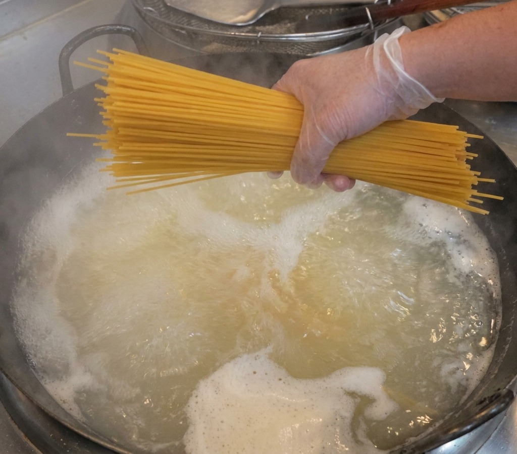 Eine Hand hält ein Bündel trockene Spaghetti über einen Topf mit dampfendem, kochendem Wasser.