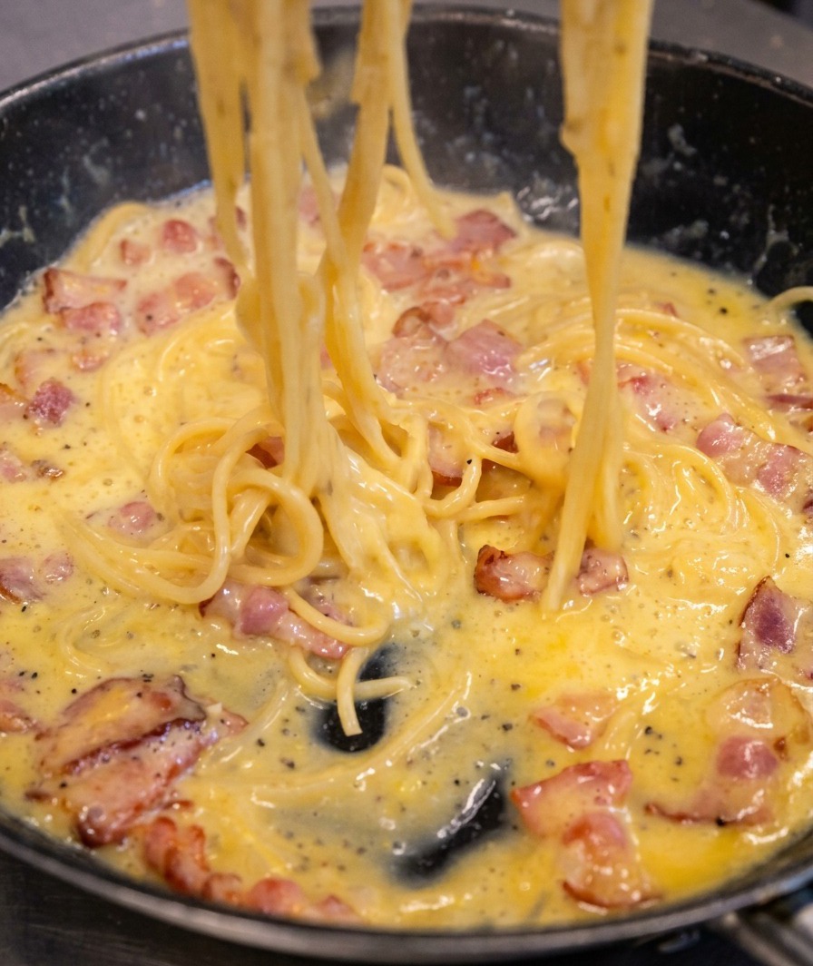 Spaghetti werden in der Pfanne geschwenkt, während sich die Sauce in einen cremigen Überzug verwandelt.