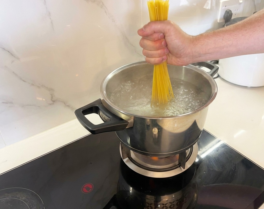 Spaghetti werden vorsichtig in kochendes Salzwasser gedrückt.