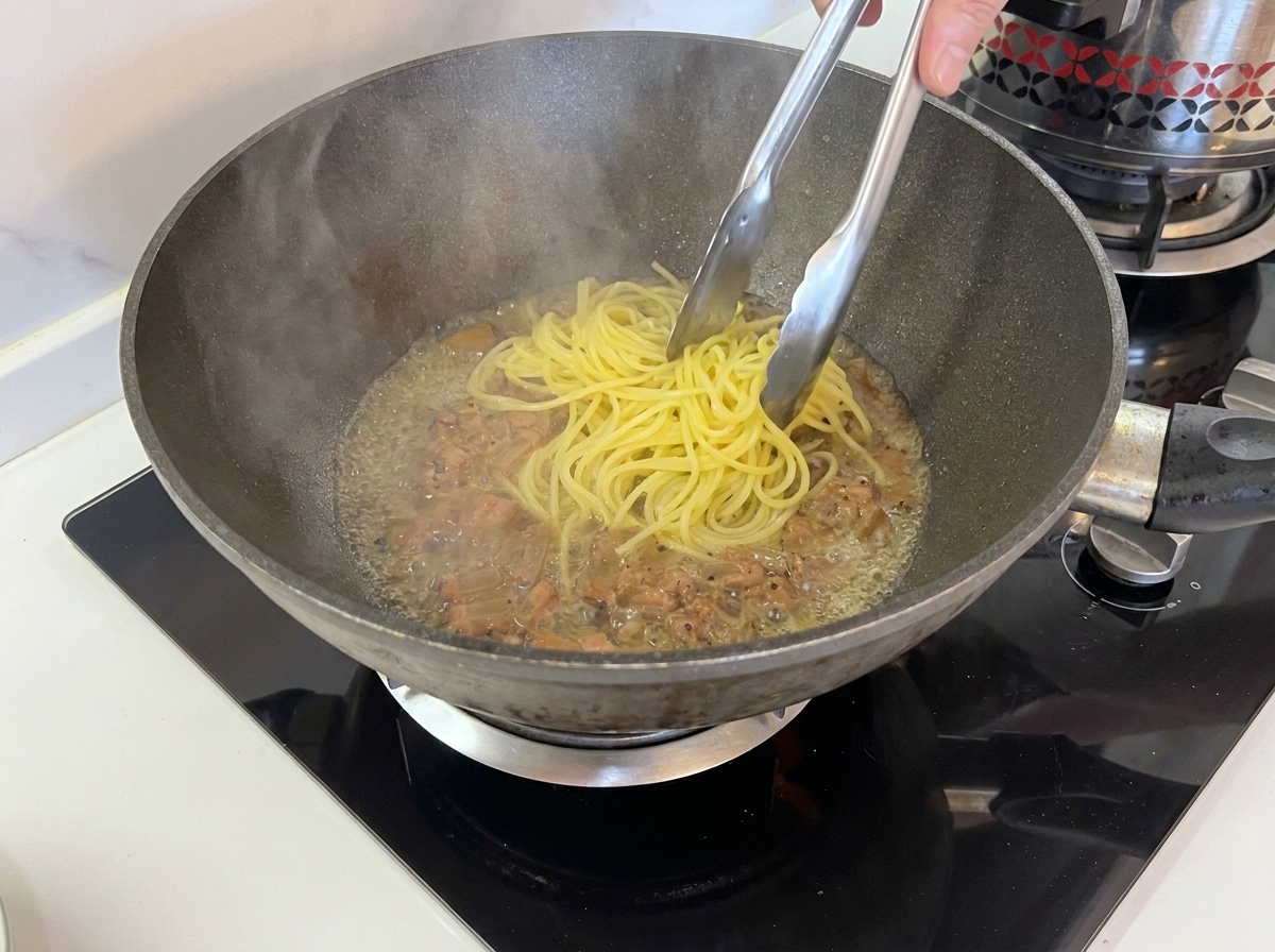 Gekochte Spaghetti werden mit einer Zange direkt in die Pfanne gehoben.