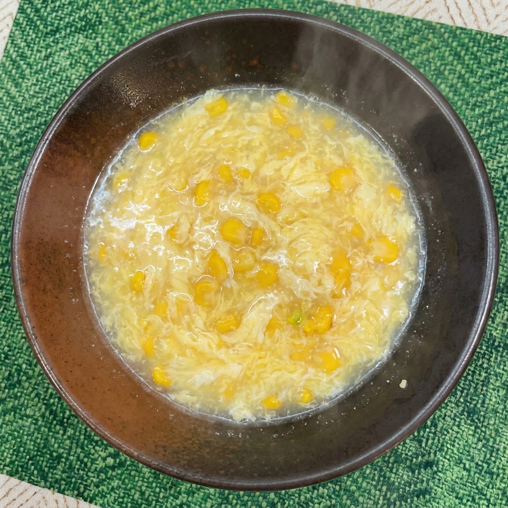 Eine cremige, hellgelbe Brühe mit Maiskörnern in einer dunklen Servierschüssel.