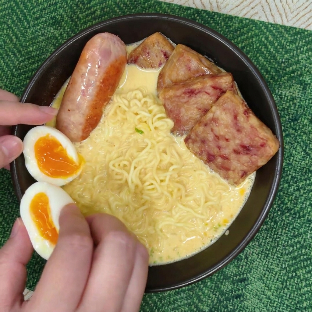 Hände legen vorsichtig zwei Hälften eines wachsweichen Eies mit leuchtend orangem Dotter in die Schüssel.