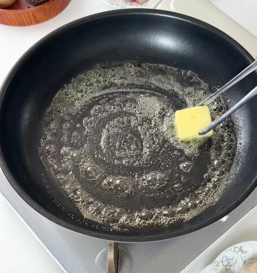 Ein Stück Butter schmilzt und sprudelt in einer schwarzen Pfanne.