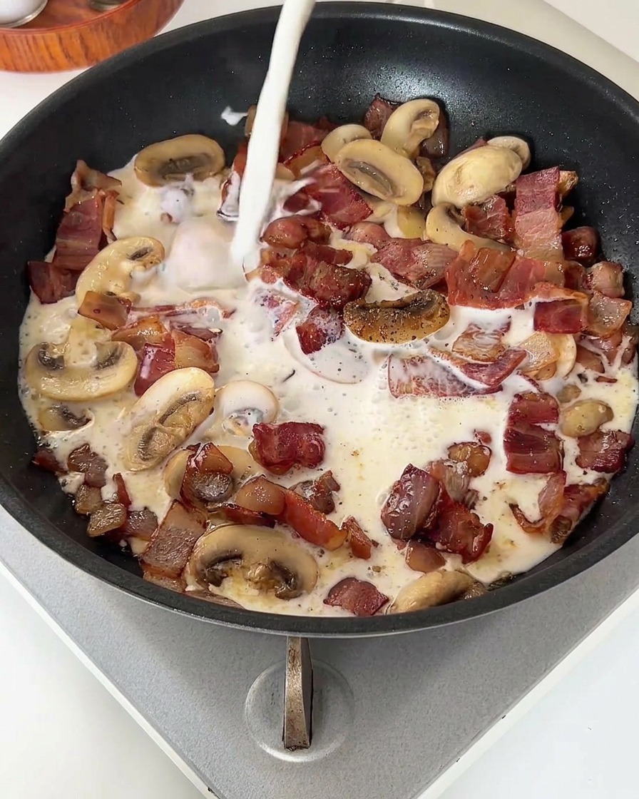 Ein Strahl Milch wird in die Pfanne mit Speck und Pilzen gegossen.
