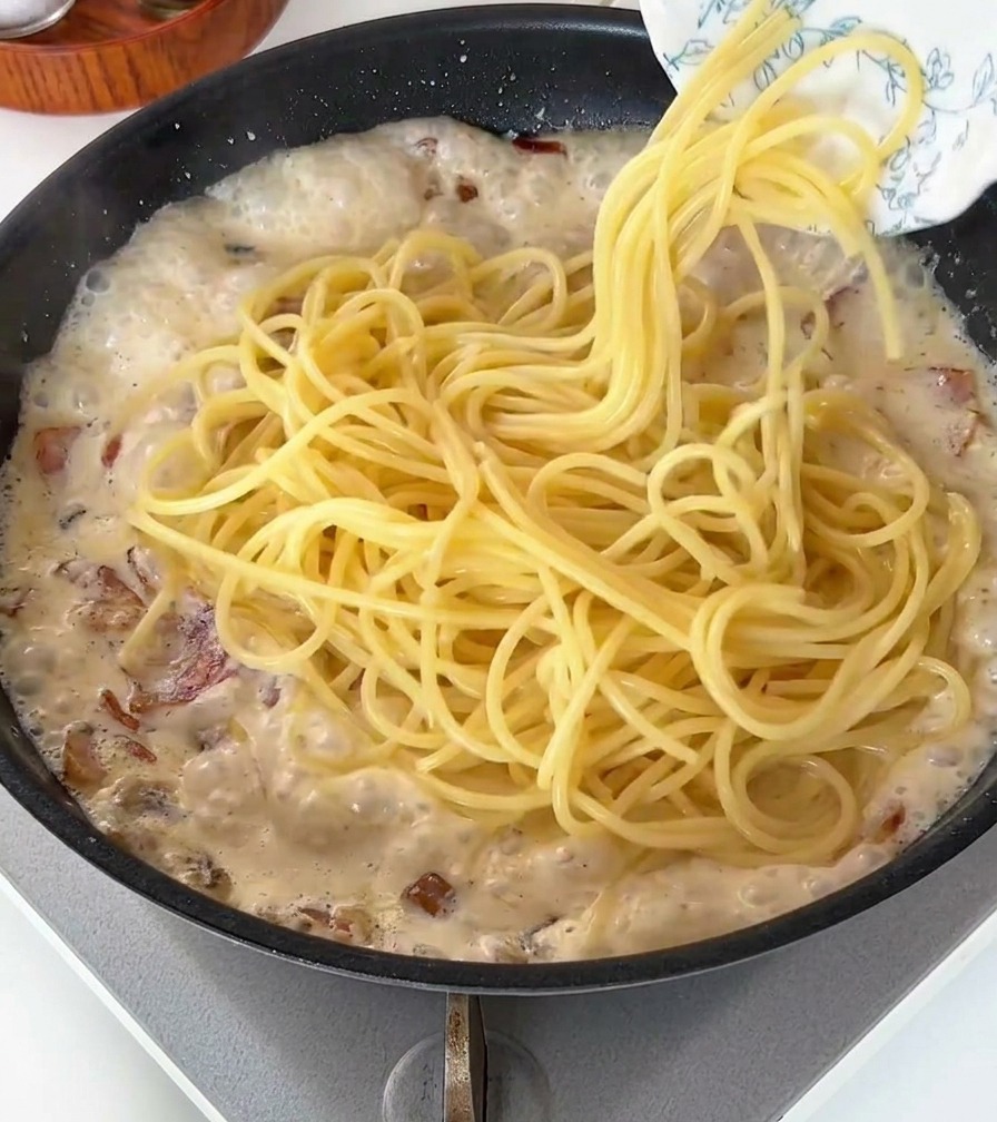 Gekochte Spaghetti werden in die sprudelnde Sahnesauce gegeben.