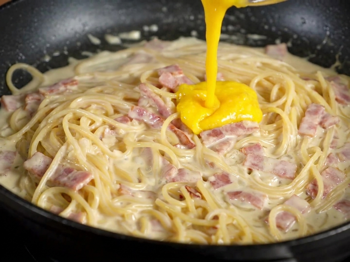 Die gelbe Eigelb-Parmesan-Mischung wird über die Pasta in der Pfanne gegossen.