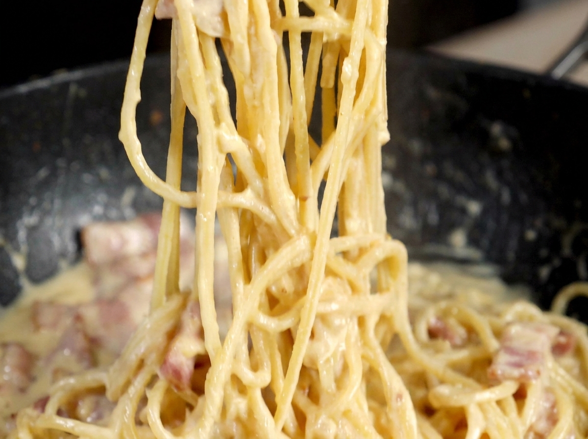 Frischer schwarzer Pfeffer wird über die fertige Carbonara gemahlen.