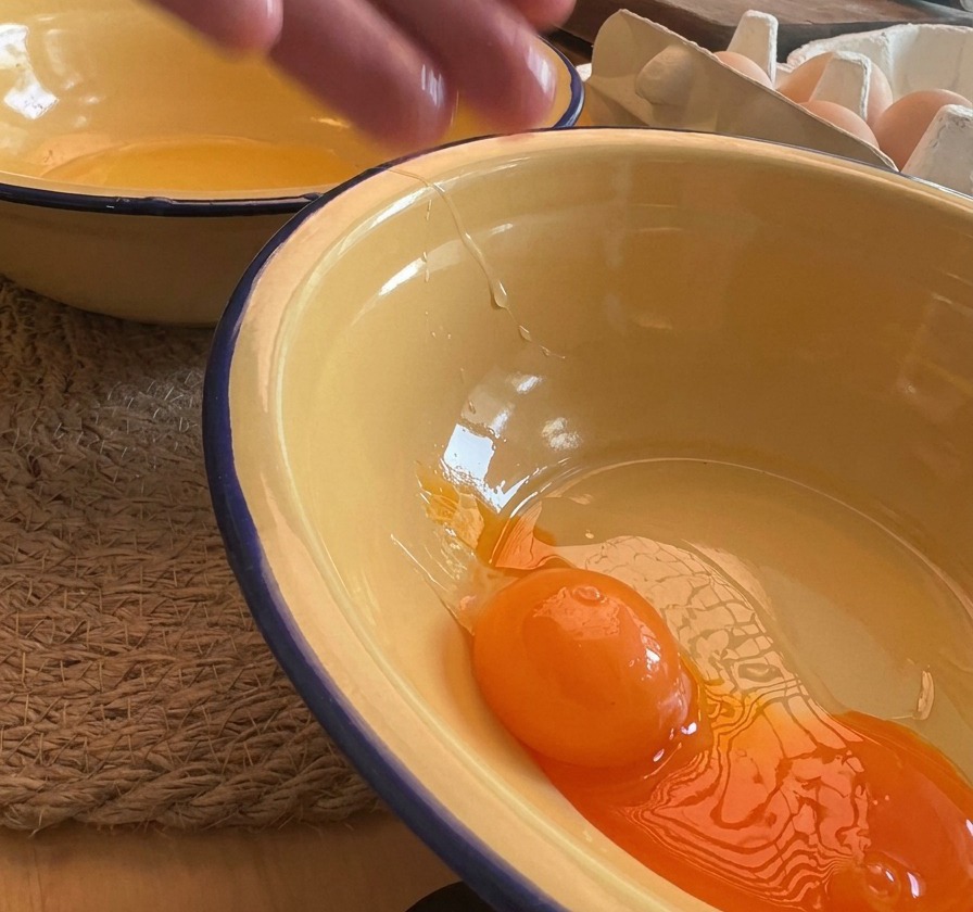 Nahaufnahme eines leuchtend orangen Eigelbs, das in eine gelbe Emailleschüssel gleitet.