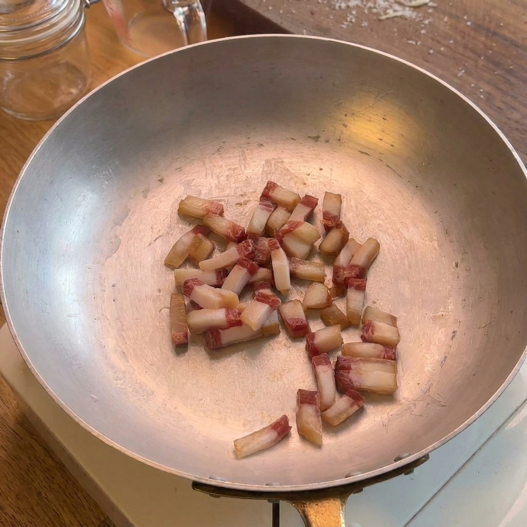 Kleine Guanciale-Würfel braten in einer weiten Edelstahlpfanne, wobei das natürliche Fett langsam austritt.