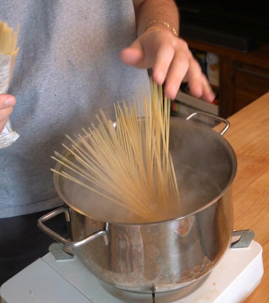 Eine Person gibt ein Bündel Spaghetti in einen Topf mit sprudelnd kochendem Wasser.