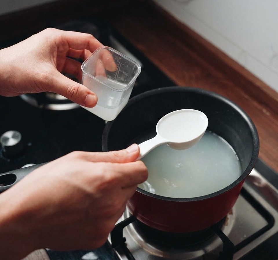 Eine weiße Schöpfkelle entnimmt trübes Nudelwasser aus einem kochenden roten Topf.