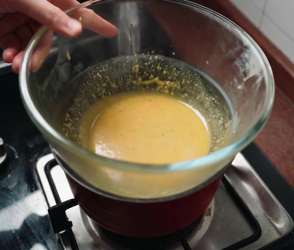 Eine Glasschüssel mit gelber Sauce wird über einen dampfenden Topf mit heißem Wasser gehalten.