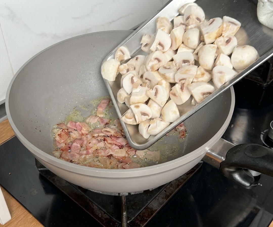 Geviertelte Pilze werden zum bratenden Speck in die Pfanne gegeben.
