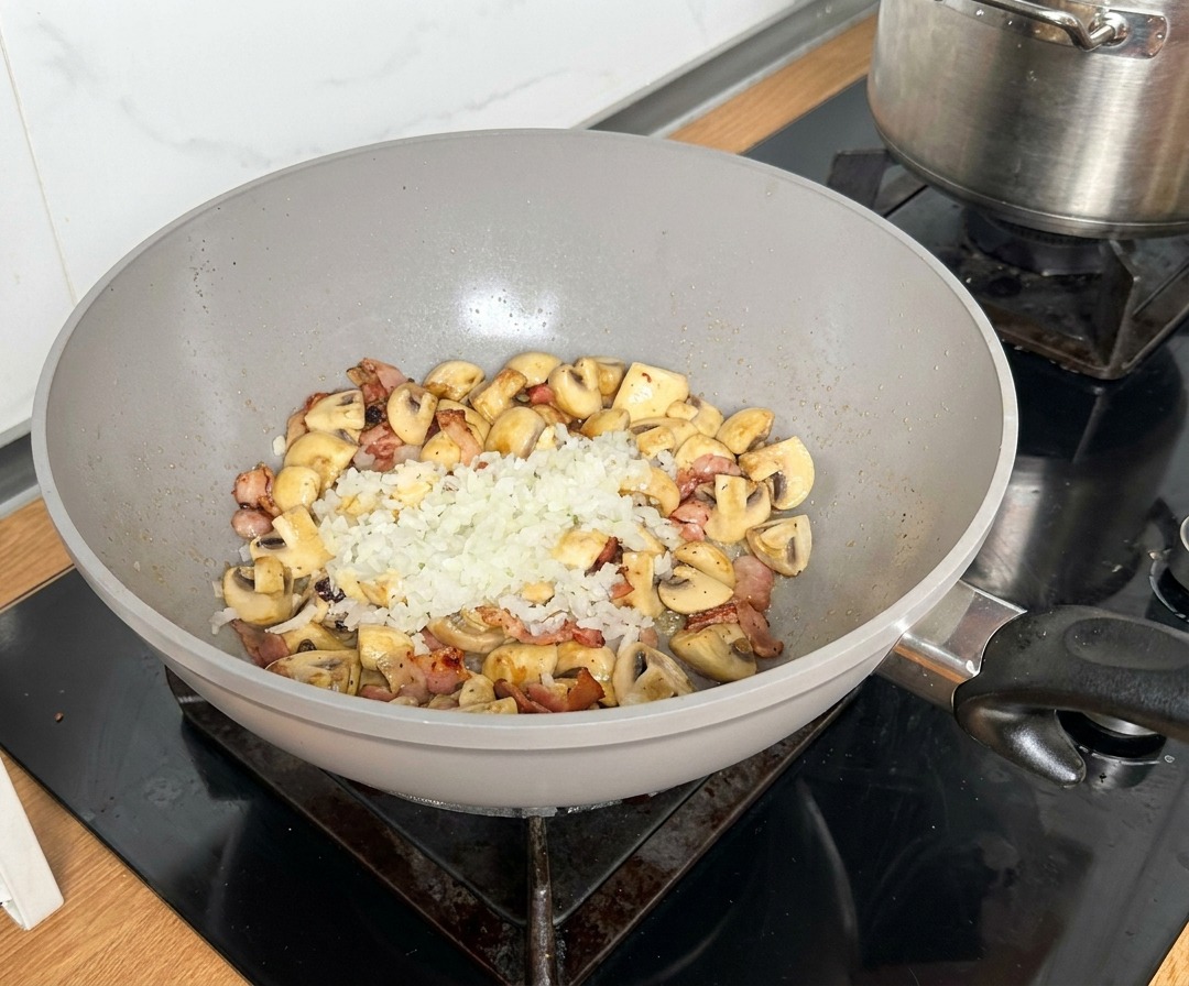 Zwiebelwürfel werden in der Pfannenmitte mit Speck und Pilzen gedünstet.