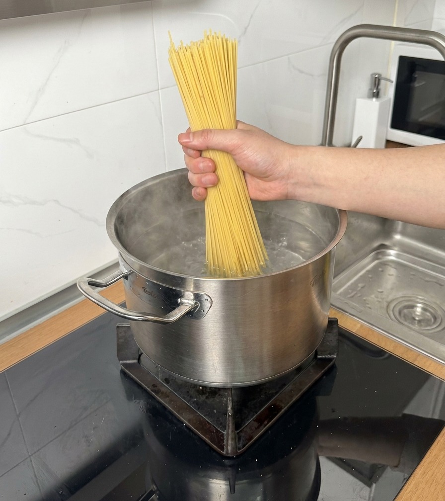 Trockene Spaghetti werden in einen Topf mit kochendem Wasser gegeben.