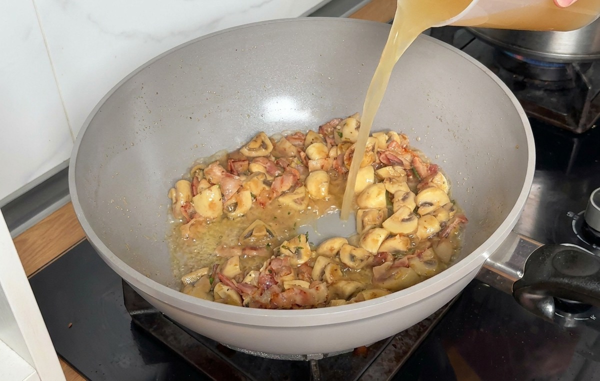 Hühnerbrühe wird aus einem Messbecher in die Pfanne gegossen.