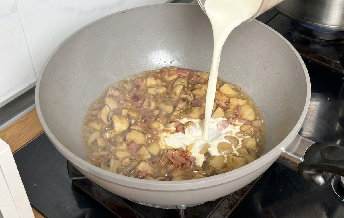 Schlagsahne wird zu der köchelnden Brühe und den Pilzen gegossen.