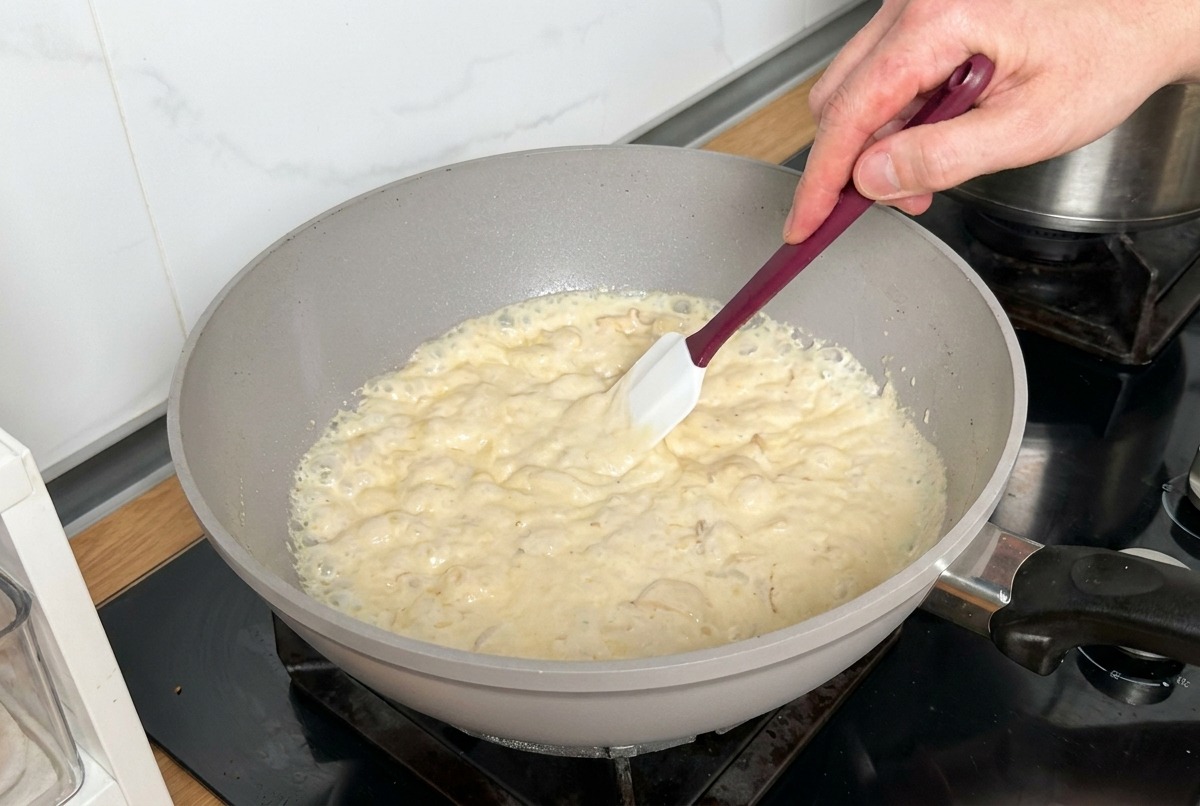 Eine sämige Sahnesauce wird mit einem weißen Pfannenwender umgerührt.