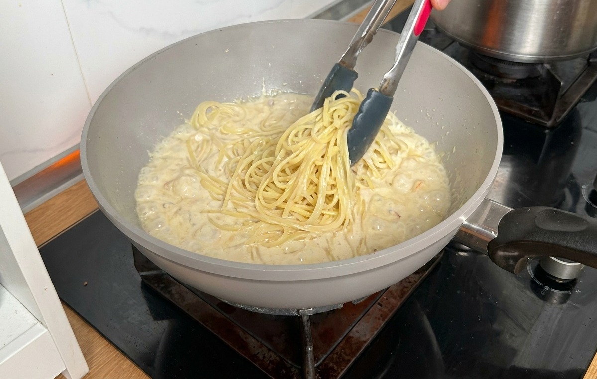 Lange Nudeln werden mit einer Zange direkt in die Pfanne mit Sauce gehoben.