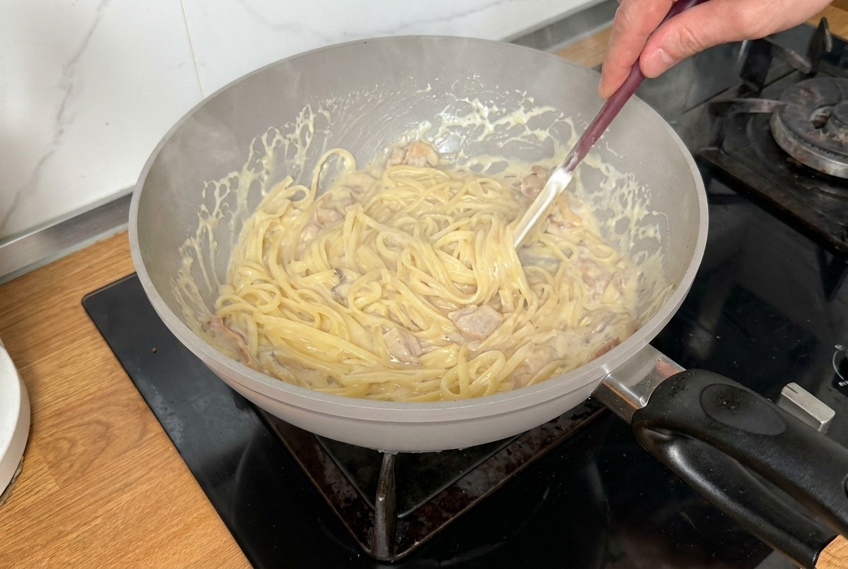 Pasta wird in der Pfanne geschwenkt, um sie gleichmäßig mit Sauce zu bedecken.